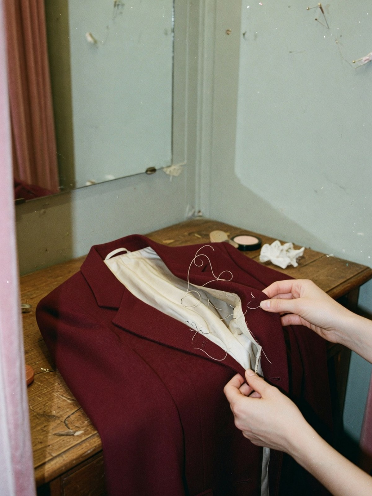 Gros plan de deux mains pinçant le revers d'un blazer bordeaux pour vérifier la présence d'un entoilage cousu