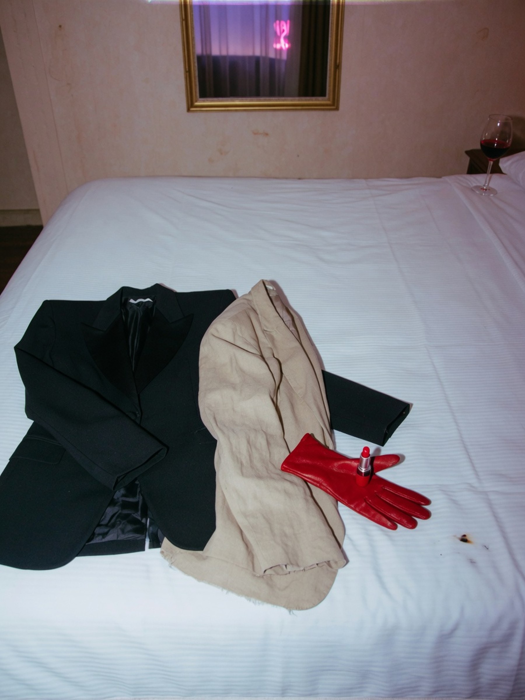 Un blazer structuré noir et un blazer souple en lainage clair posés côte à côte sur un lit d'hôtel, lumière de fin de journée.