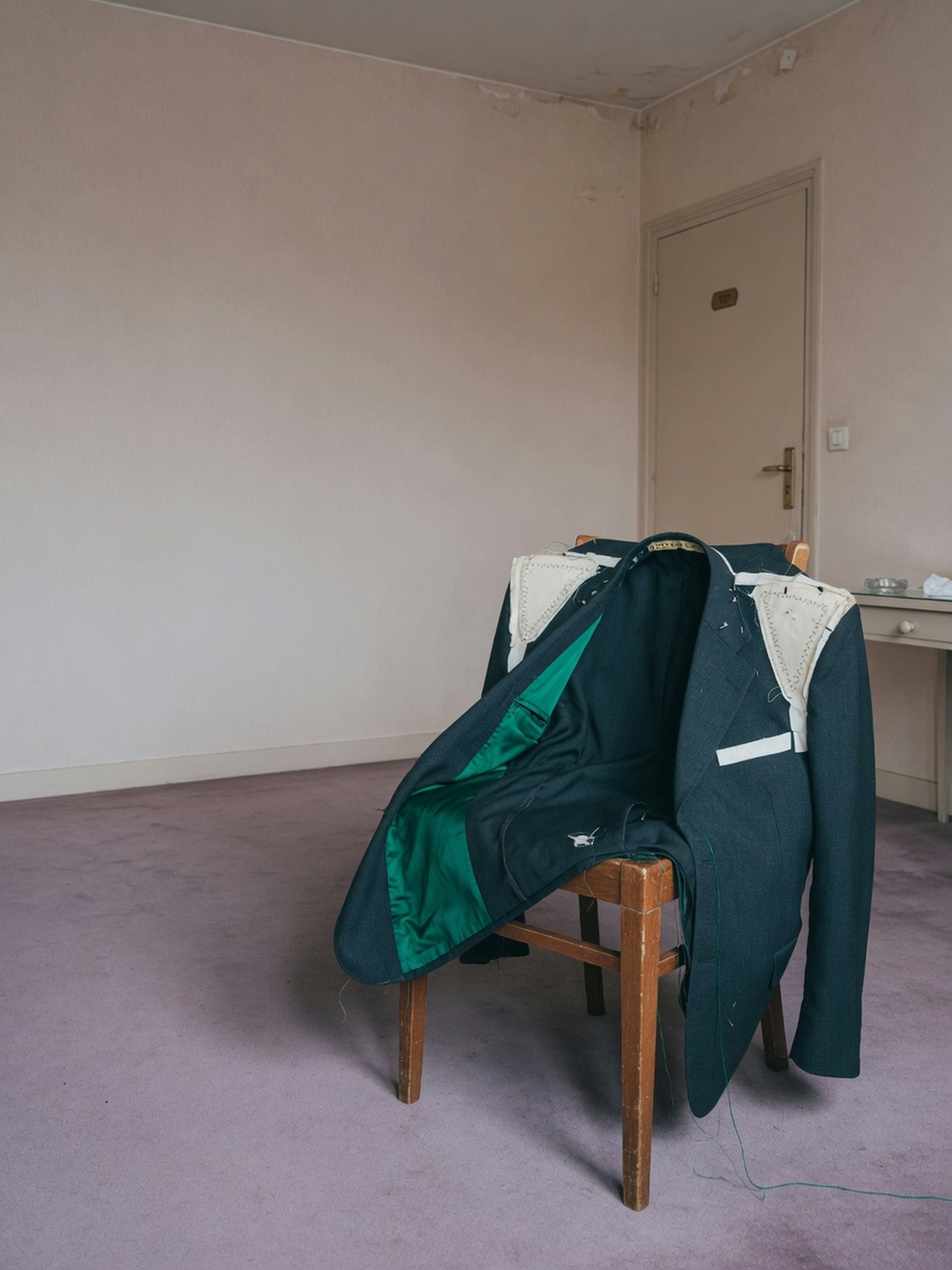 Blazer ouvert sur un dossier de chaise, éclairage flash révélant l'épaulette et la doublure intérieure, décor de chambre neutre.