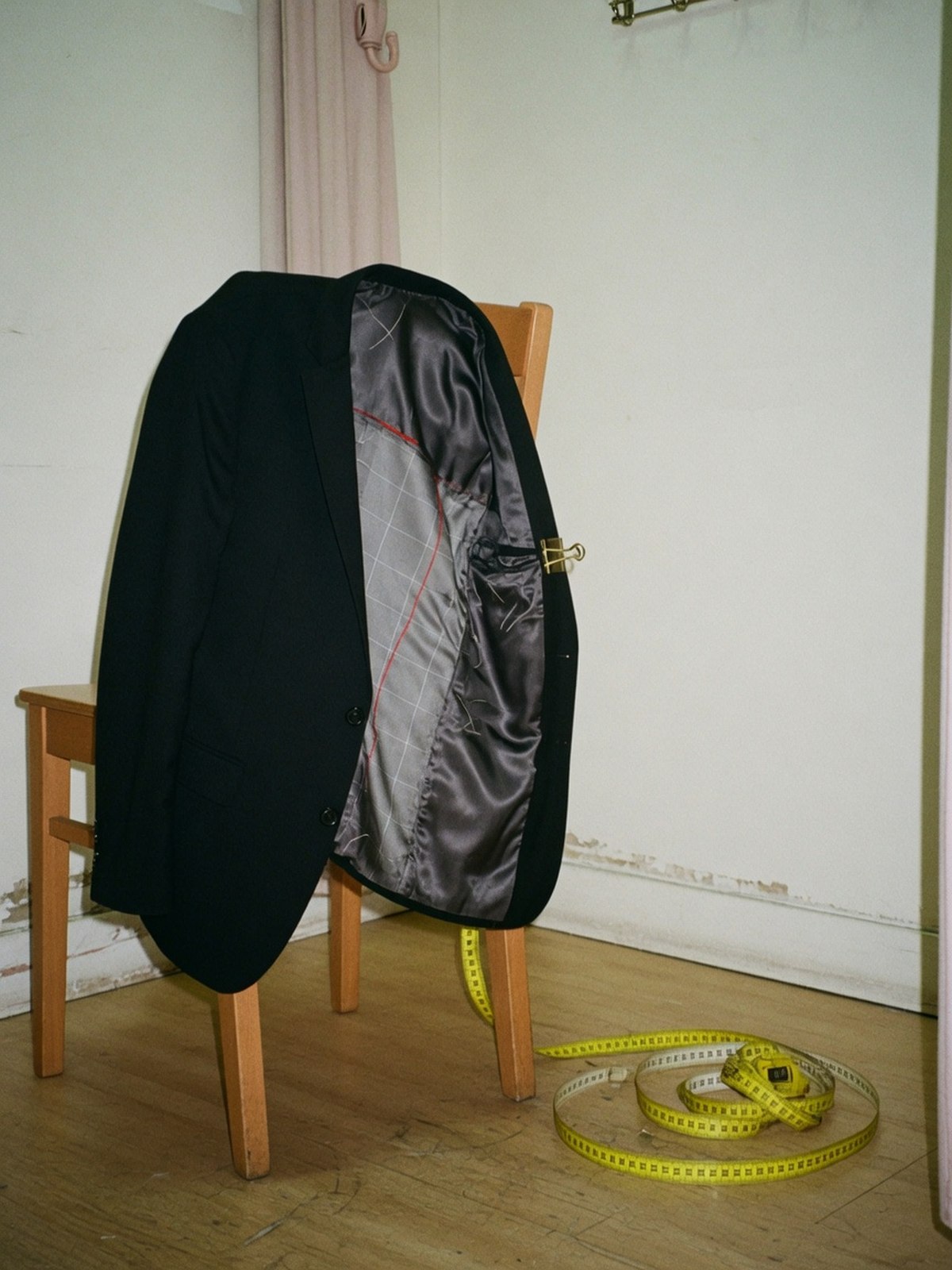 Blazer noir sur un cintre en bois, doublure maintenue ouverte par une pince révélant la toile d'entoilage intérieure