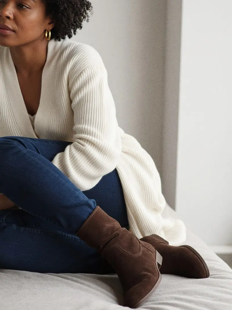 Illustration, mannequin fictif : Détail des jambes d'une femme, jean slim indigo rentré dans des bottines en cuir velours marron foncé à tige souple.
