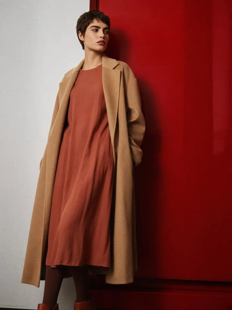 Illustration, mannequin fictif : Femme en robe midi fluide terracotta et manteau camel long, collant marron et bottines noisette à bout rond et petit talon.