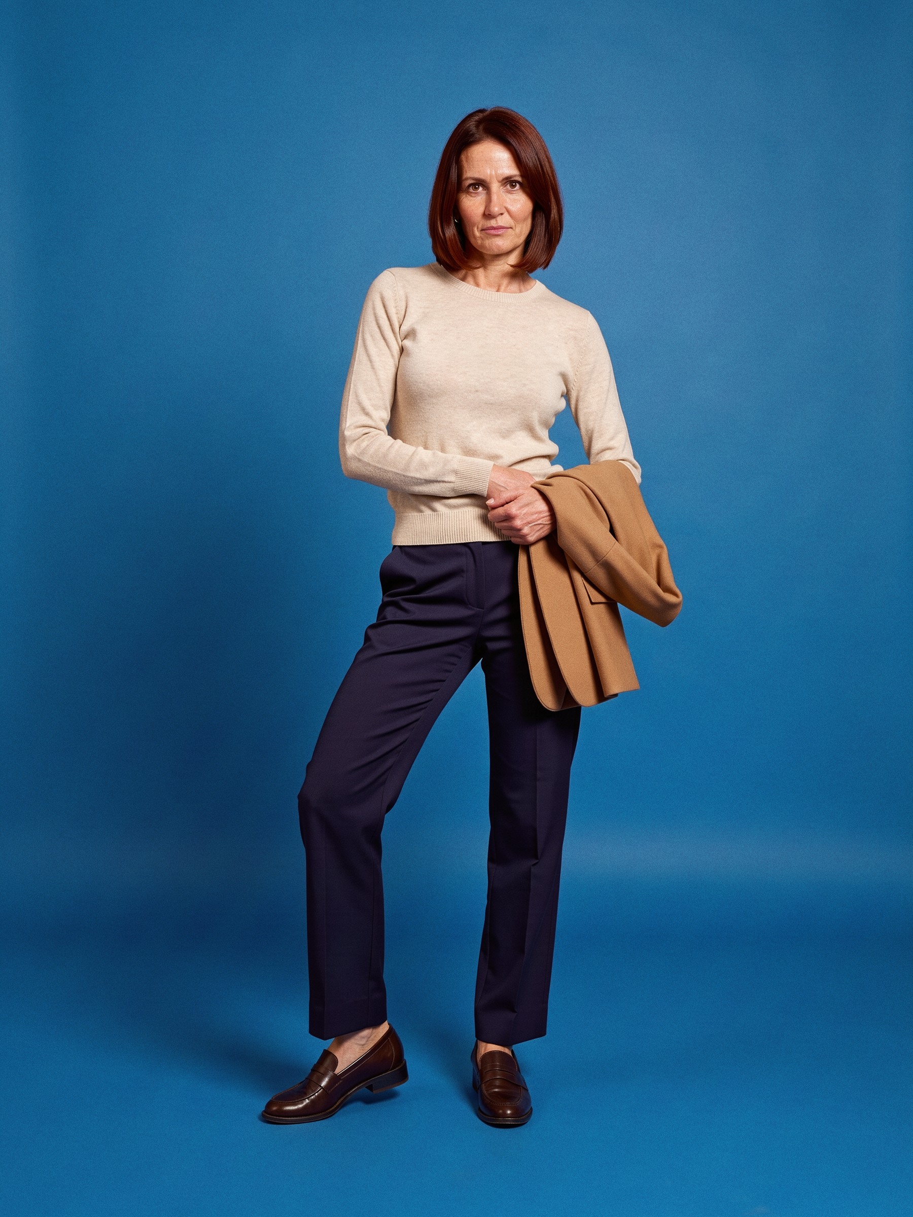 Mannequin en pantalon droit bleu marine, maille fine écrue et mocassins, debout dans un couloir de bureau vide