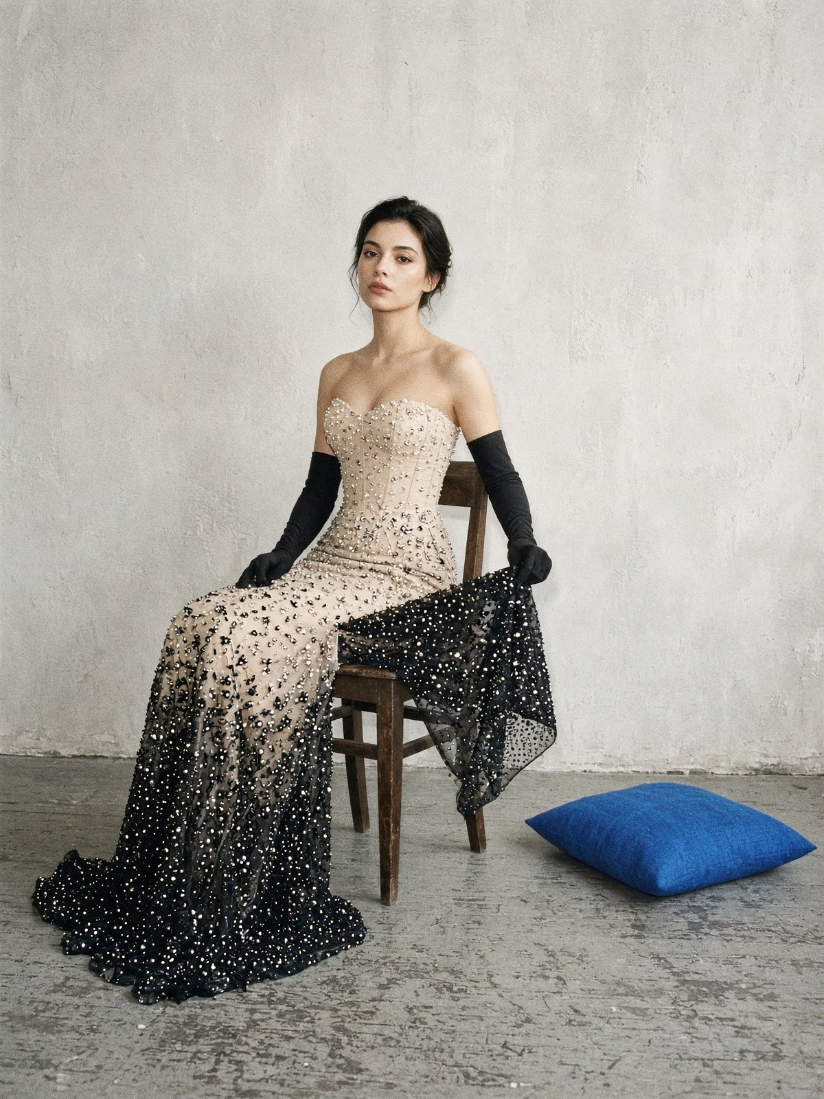Mannequin assise soulevant l'ourlet d'une robe noire brodée de perles en dégradé pour en montrer l'envers