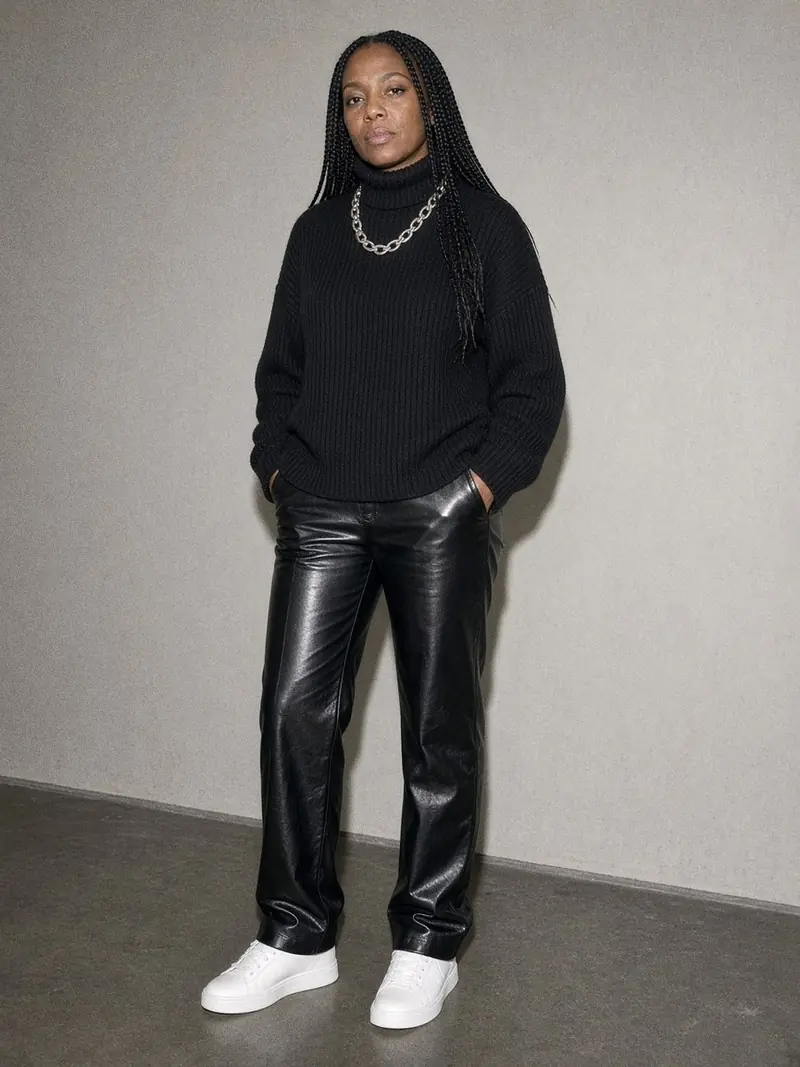Illustration, mannequin fictif : Femme en gros col roulé noir côtelé, pantalon en cuir noir et baskets blanches, vue en pied.