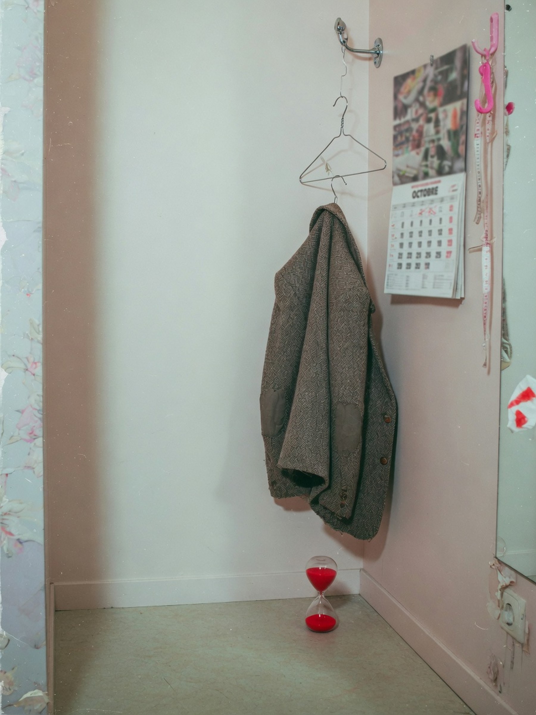 Nature morte éditoriale : une veste en tweed sur cintre dans une boutique vide, lumière de flash, une touche de rouge, calendrier flou en arrière-plan.