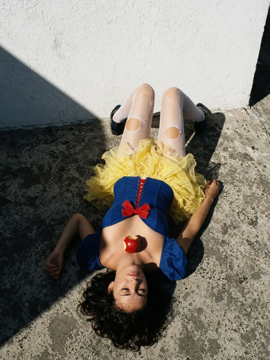 Déguisement Blanche-Neige trash, corset bleu, tutu jaune et pomme croquée, allongée au soleil