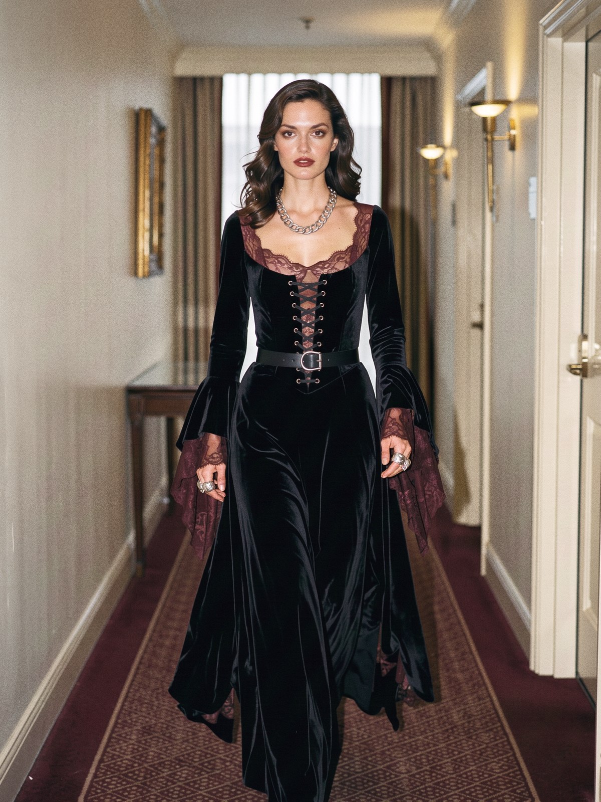 Mannequin en robe de velours noir, ceinture large et bijoux argentés imposants dans un couloir