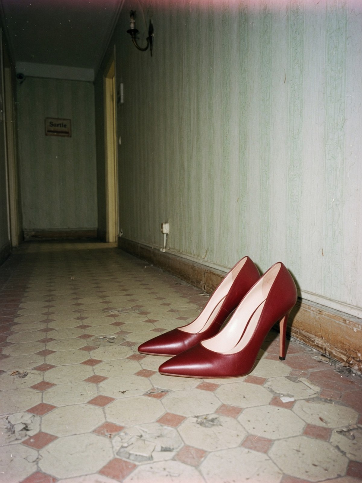 Paire d'escarpins à empeigne remontée et pointue posée au sol dans un couloir carrelé, éclairée au flash.