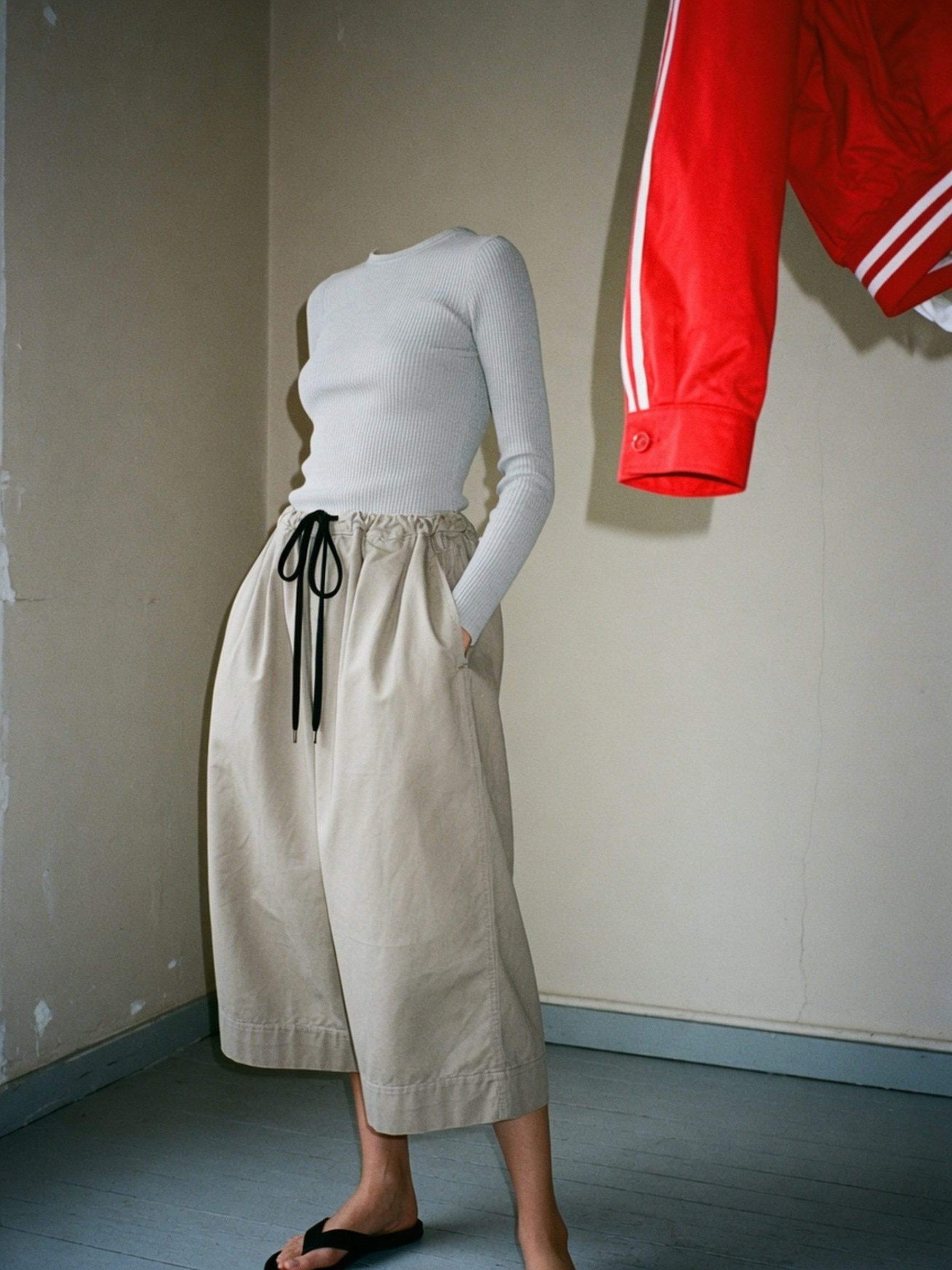 Culotte-jupe ample en toile beige portée avec un pull fin, cadrage taille jusqu'aux genoux, lumière de studio froide