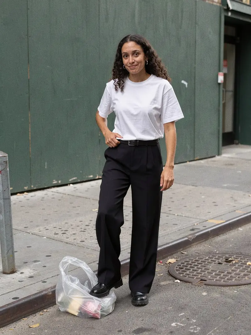 Illustration, mannequin fictif : Femme en tee-shirt blanc ample et épais rentré dans un pantalon noir large, marchant dans une rue animée.
