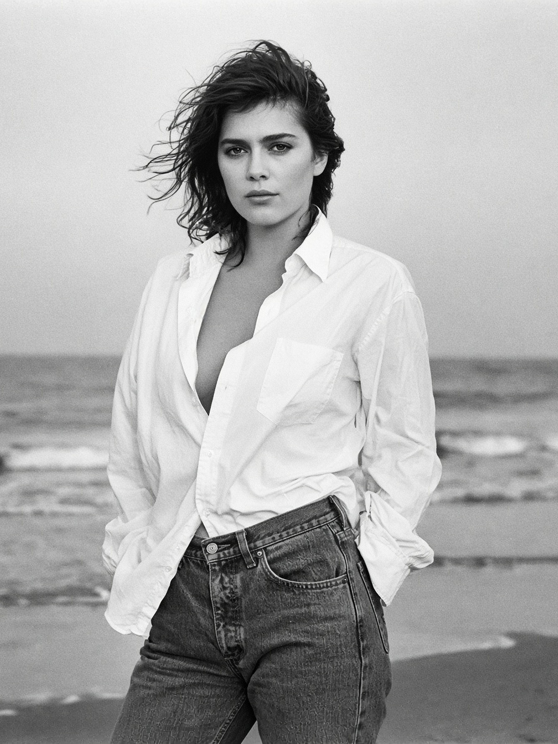 Femme en chemise blanche d'homme et jean, sur une plage venteuse, en noir et blanc