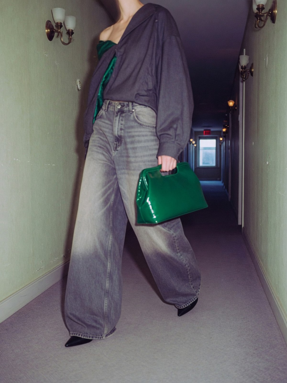 Une silhouette élancée portant un jean large XXL à taille haute, volume ample jusqu'au sol, dans un couloir en fin de journée.