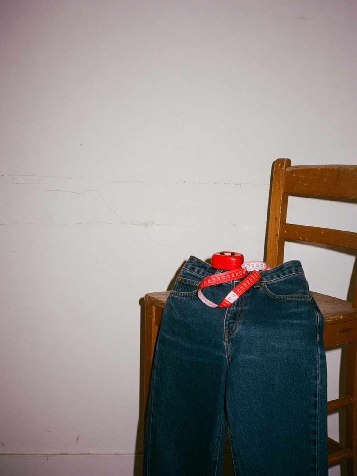 Détail d'un jean droit taille haute en denim foncé avec un mètre ruban posé sur la ceinture