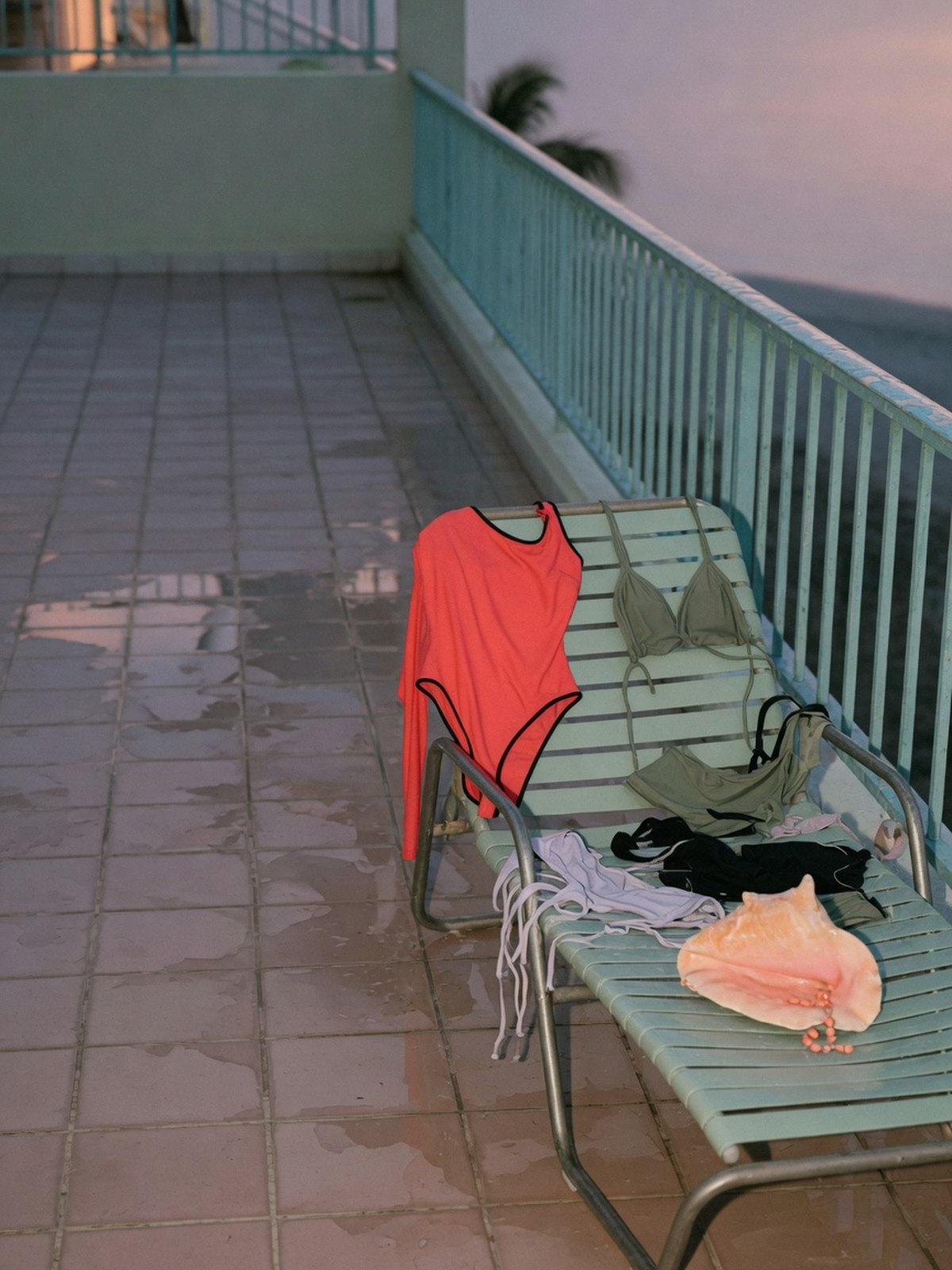 Nature morte de maillots de bain de la capsule Etam x Hôtel Mahfouf disposés au bord d'une piscine au crépuscule.