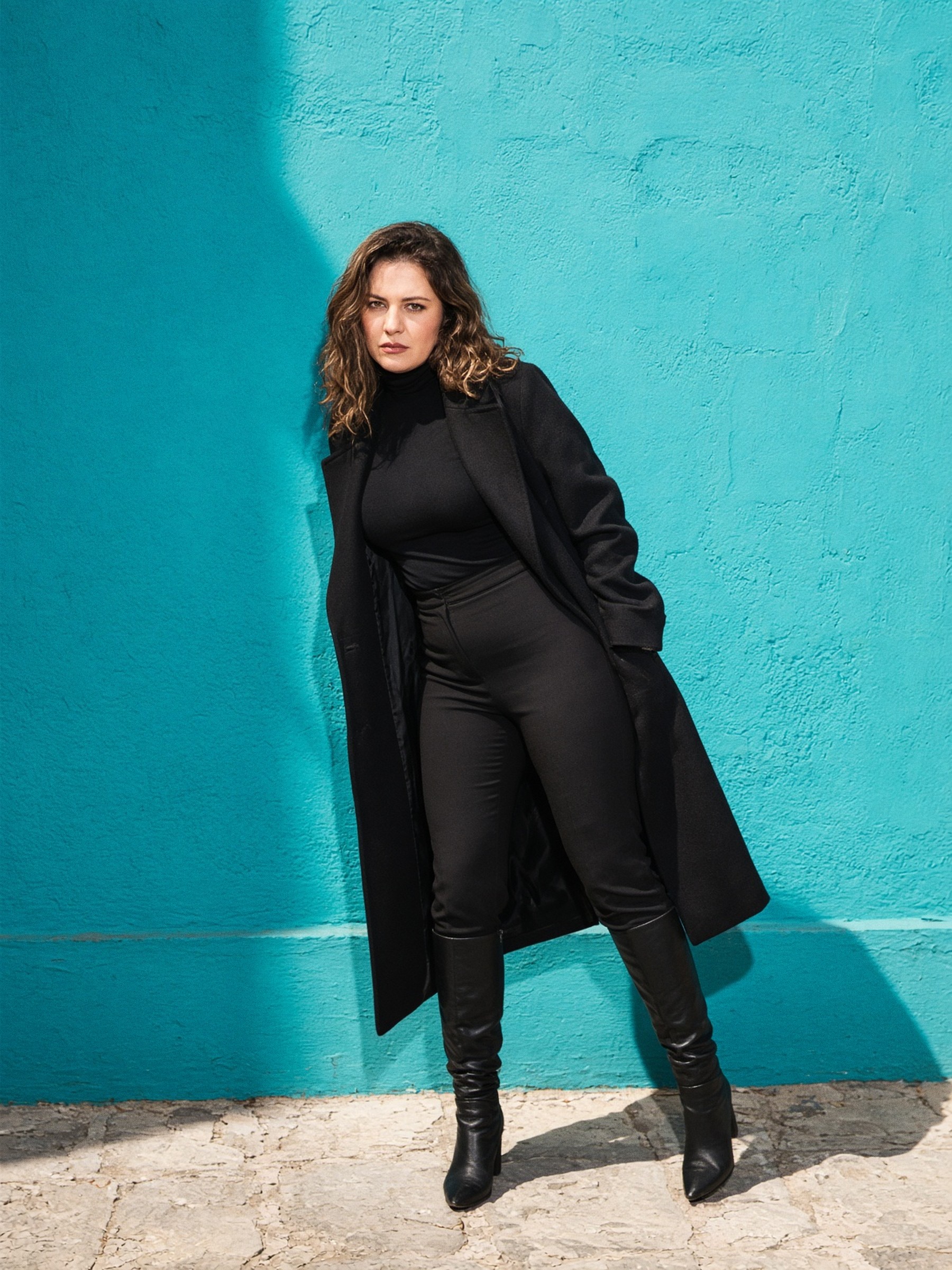 Mannequin en manteau long noir et bottes hautes noires, debout dans un couloir d'hôtel, lumière au flash