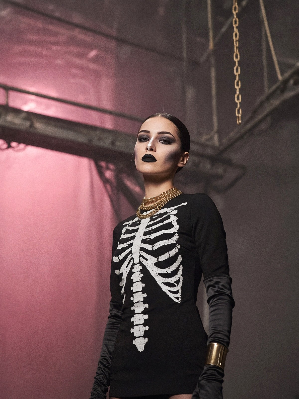 Mannequin au maquillage graphique noir et blanc, gants longs noirs, manchette et chaînes dorées, dans une coulisse de théâtre