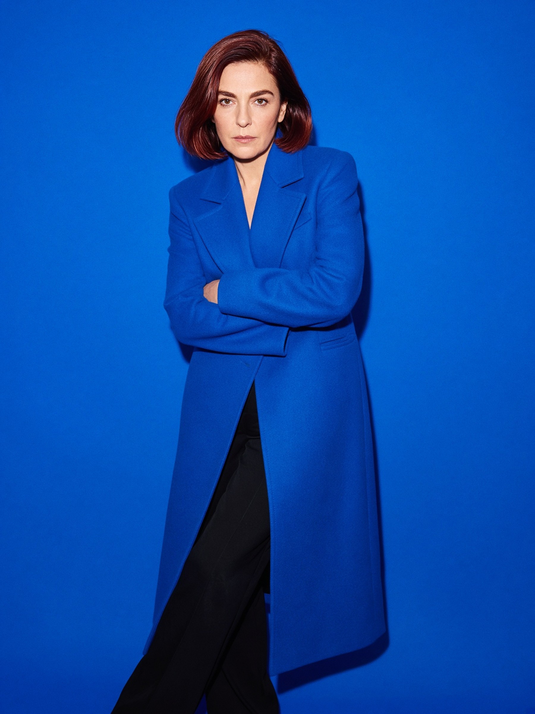 Mannequin en manteau long bleu cobalt en laine mate dans un couloir d'hôtel aux tons gris
