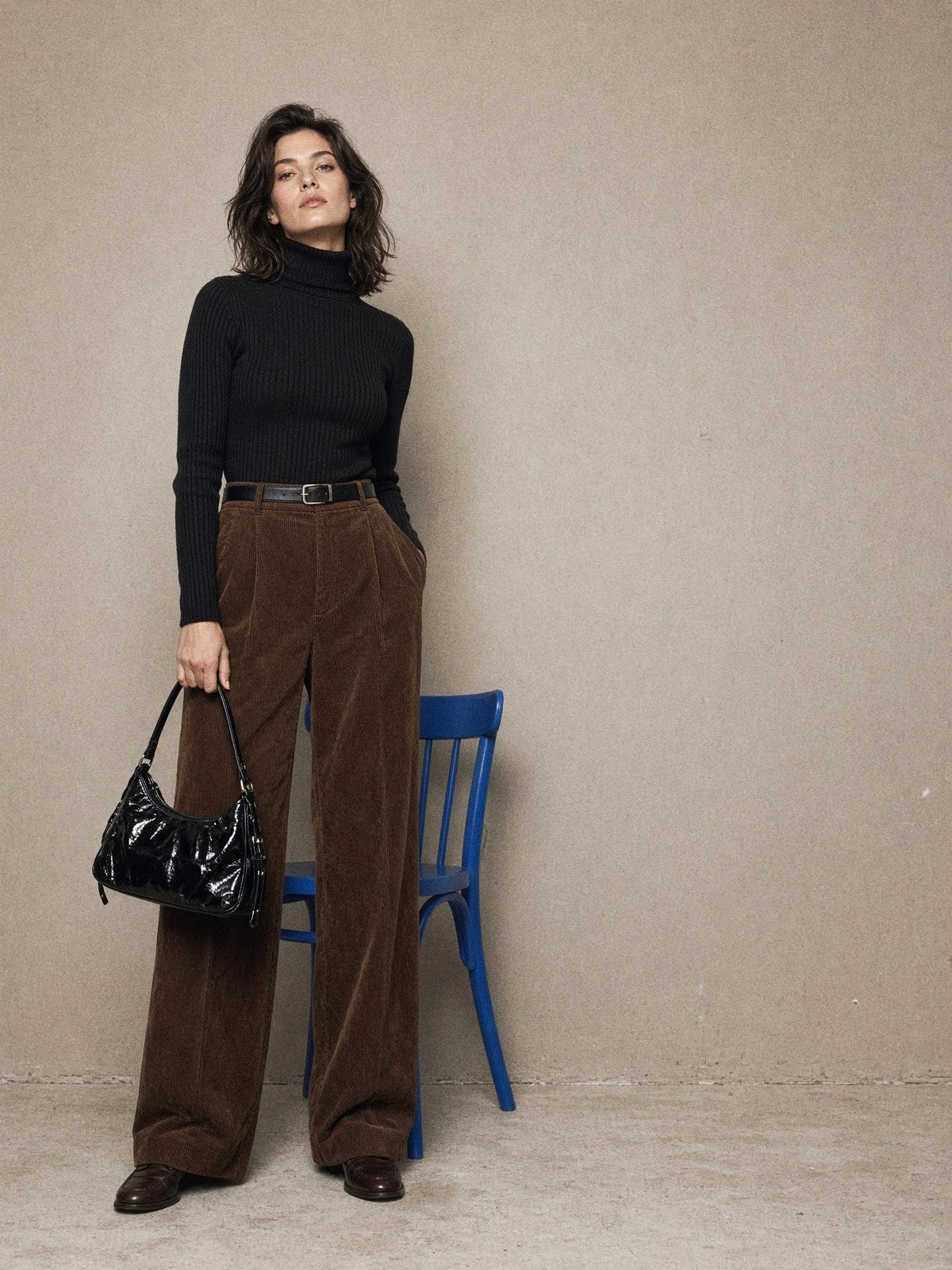 Mannequin en pantalon marron côtelé coupe barrel avec maille noire côtelée rentrée dans la taille et sac noir verni