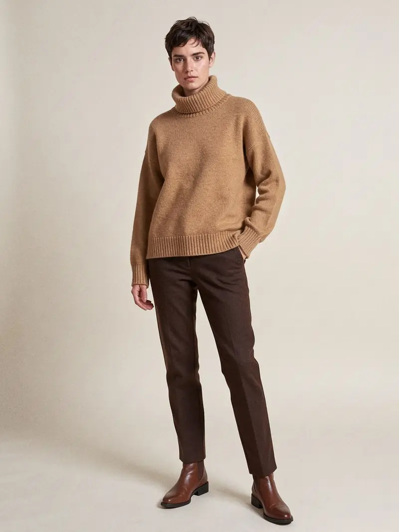 Illustration, mannequin fictif : Femme en pull cachemire épais à col roulé camel, porté sur un pantalon brun chocolat et des bottines en cuir marron.