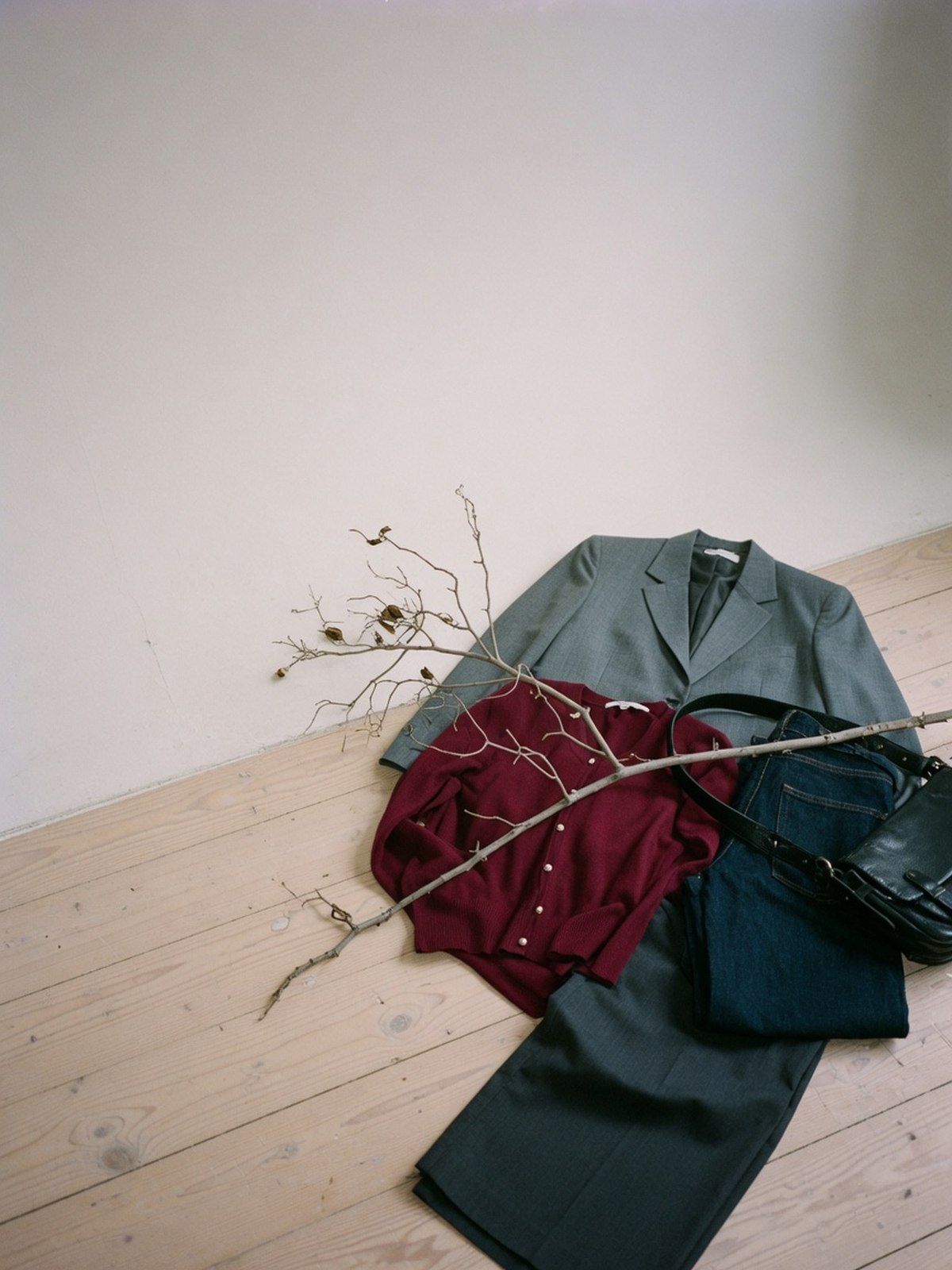 Un blazer gris boxy, un cardigan bordeaux, un jean et un pantalon large posés côte à côte au sol.
