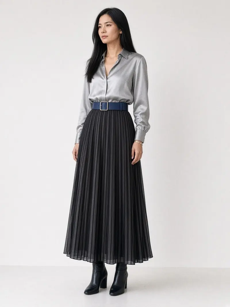 Illustration, mannequin fictif : Femme en chemise en soie gris argent et longue jupe plissée en mousseline anthracite, ceinturée d'une large ceinture en cuir bleu nuit, bottines noires.