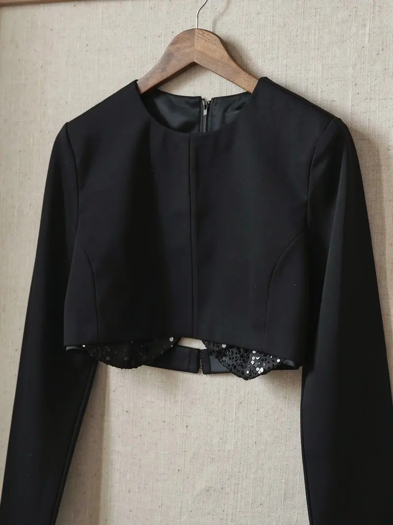 Illustration, mannequin fictif : Top court noir sur un cintre, gros plan sur la bande de sequins festonnée à l'ourlet