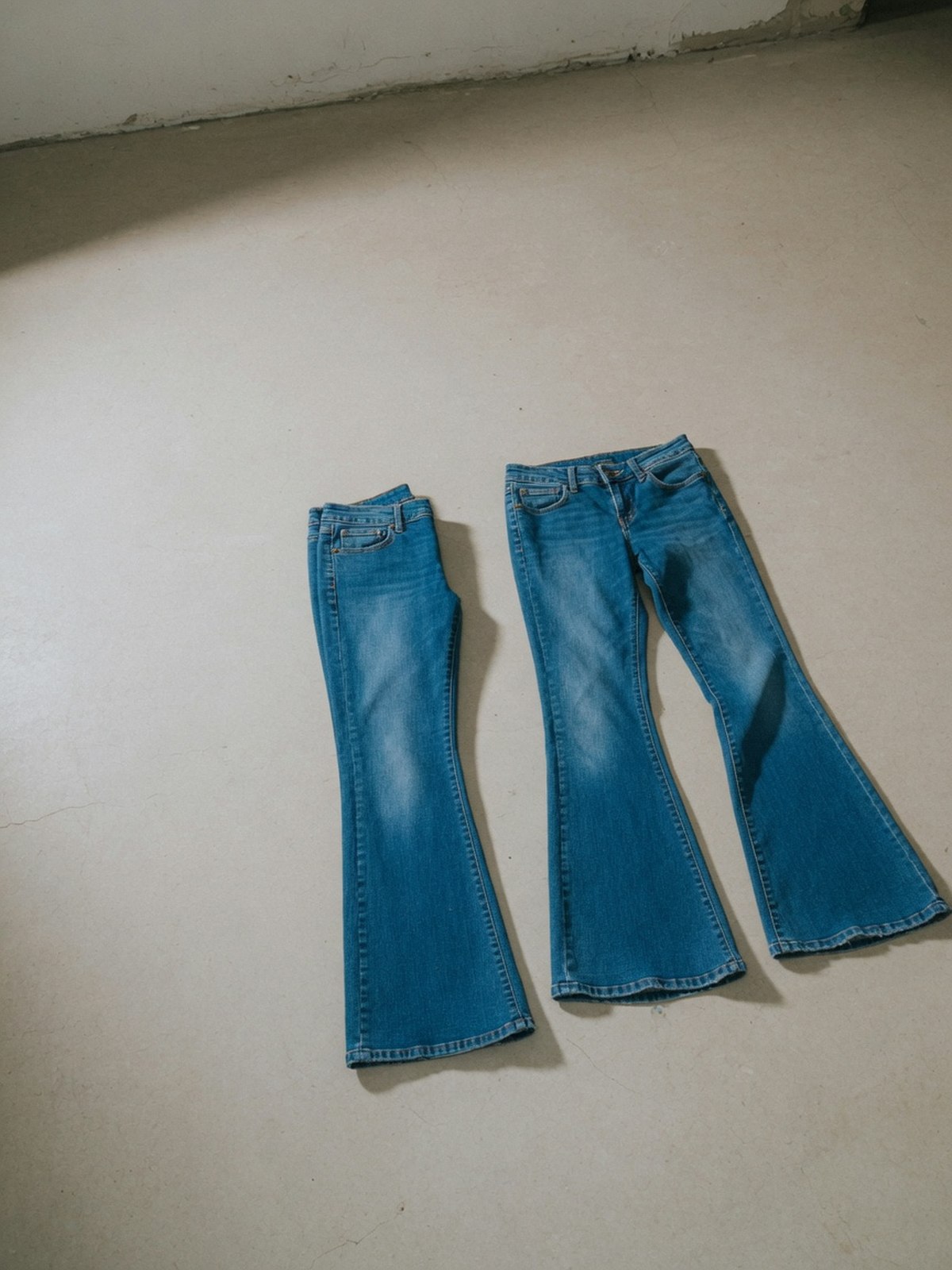 Deux jambes de jean bleu posées à plat côte à côte, l'une avec un évasement discret en bas d'ourlet, l'autre avec une ouverture plus marquée dès le mollet, illustrant la différence entre coupe straight et coupe bootcut.