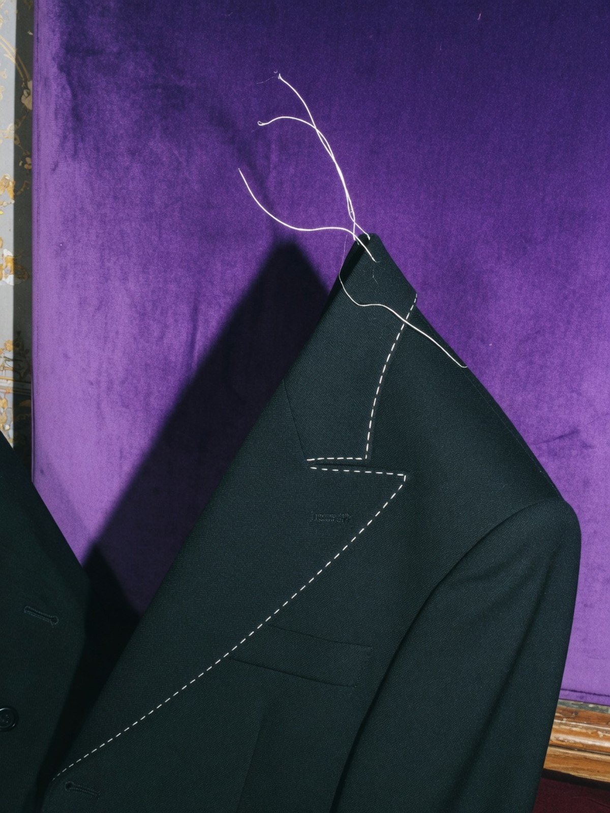 Gros plan sur un large revers de veste noire, coupe sculptée et structurée, sur fond violet.
